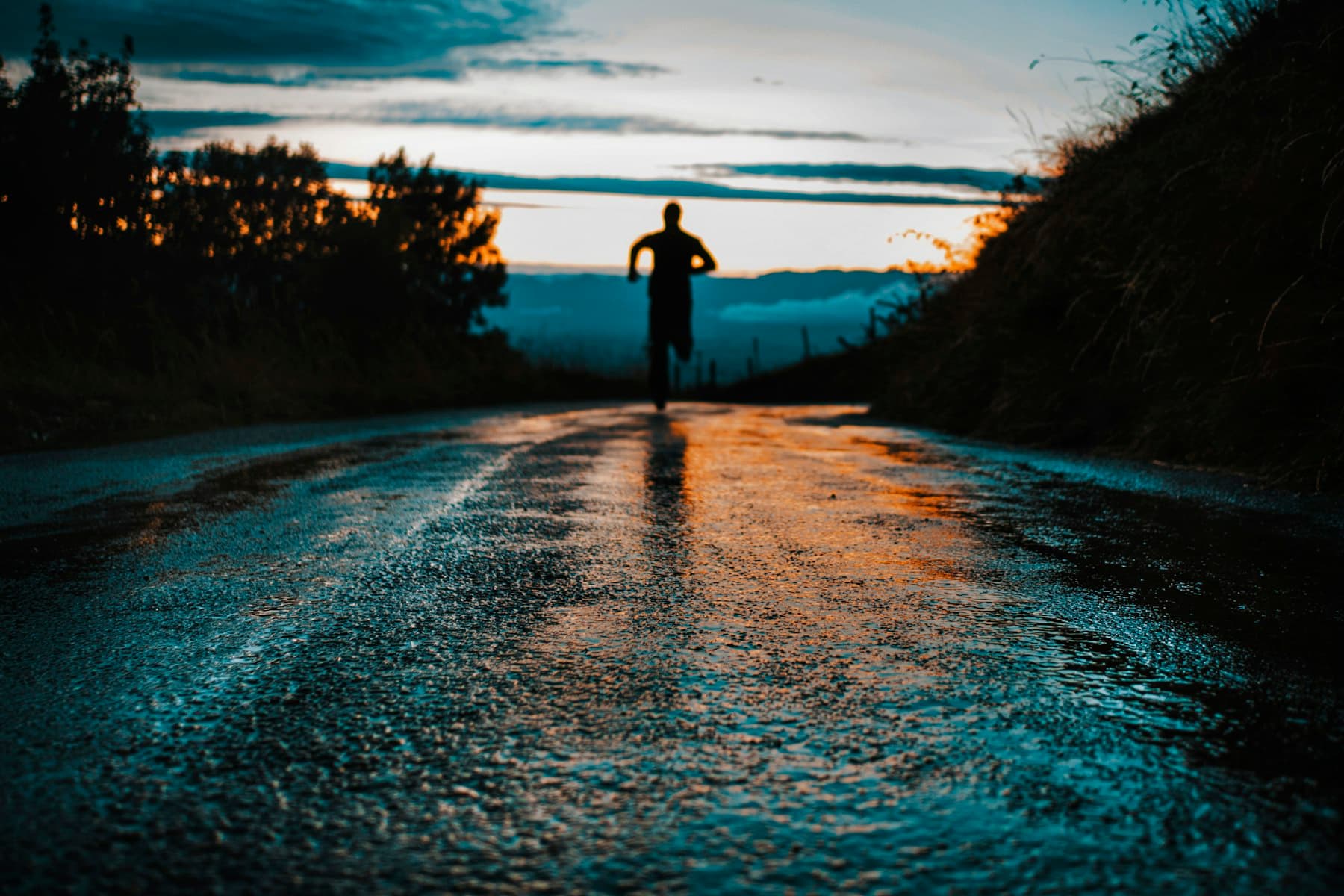 A lone runner silhouetted on a wet road as the sun comes up