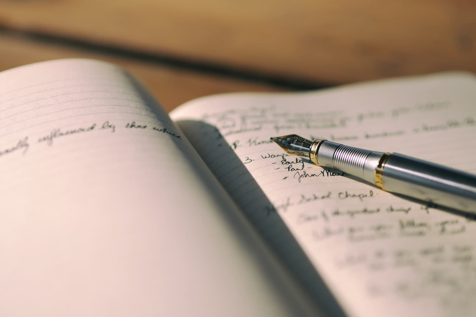 A fountain pen resting on the handwritten pages of an open notebook